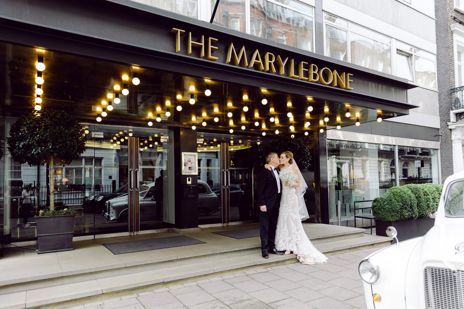 A bride and her father pose outside The Marylebone Hotel
