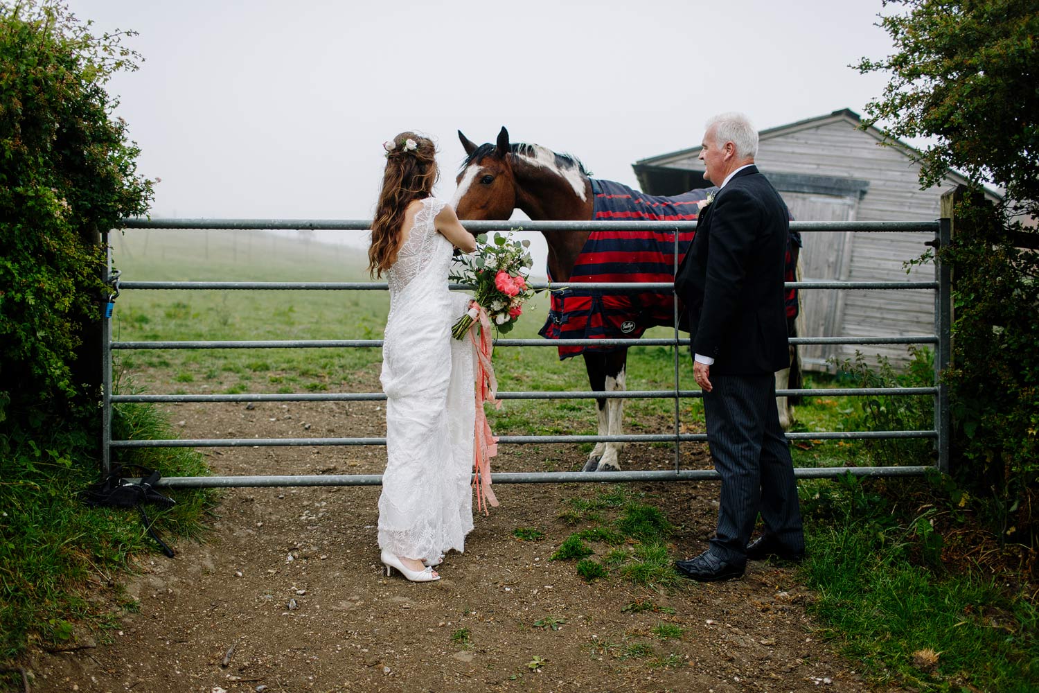 A bride and groom stand with a horse in the fog
