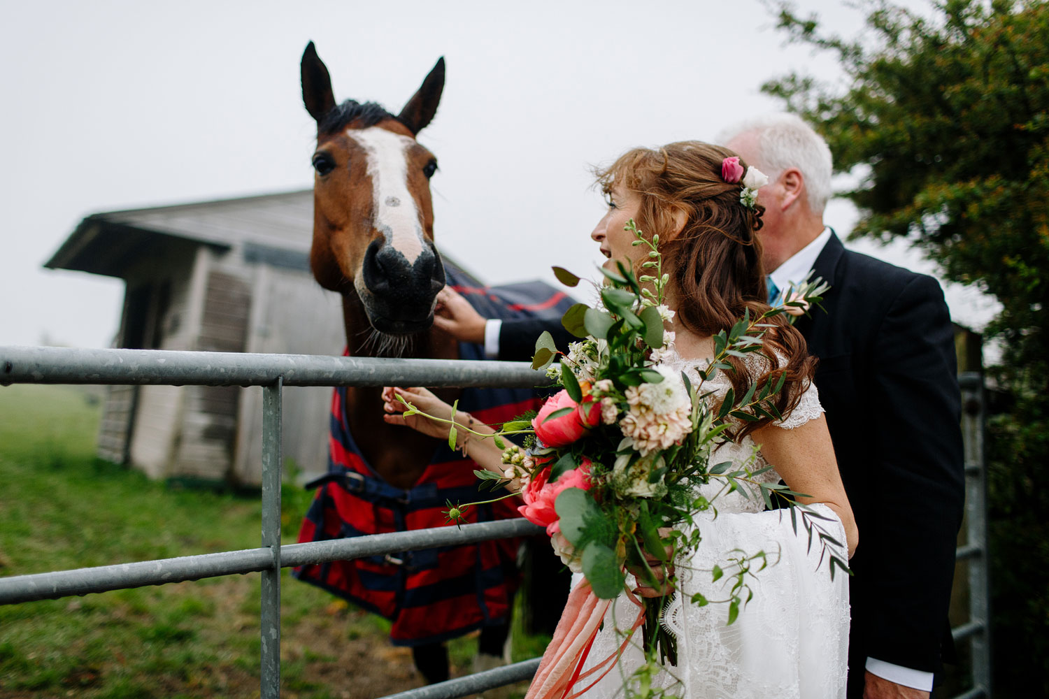 A bride and groom stand with a horse in the fog